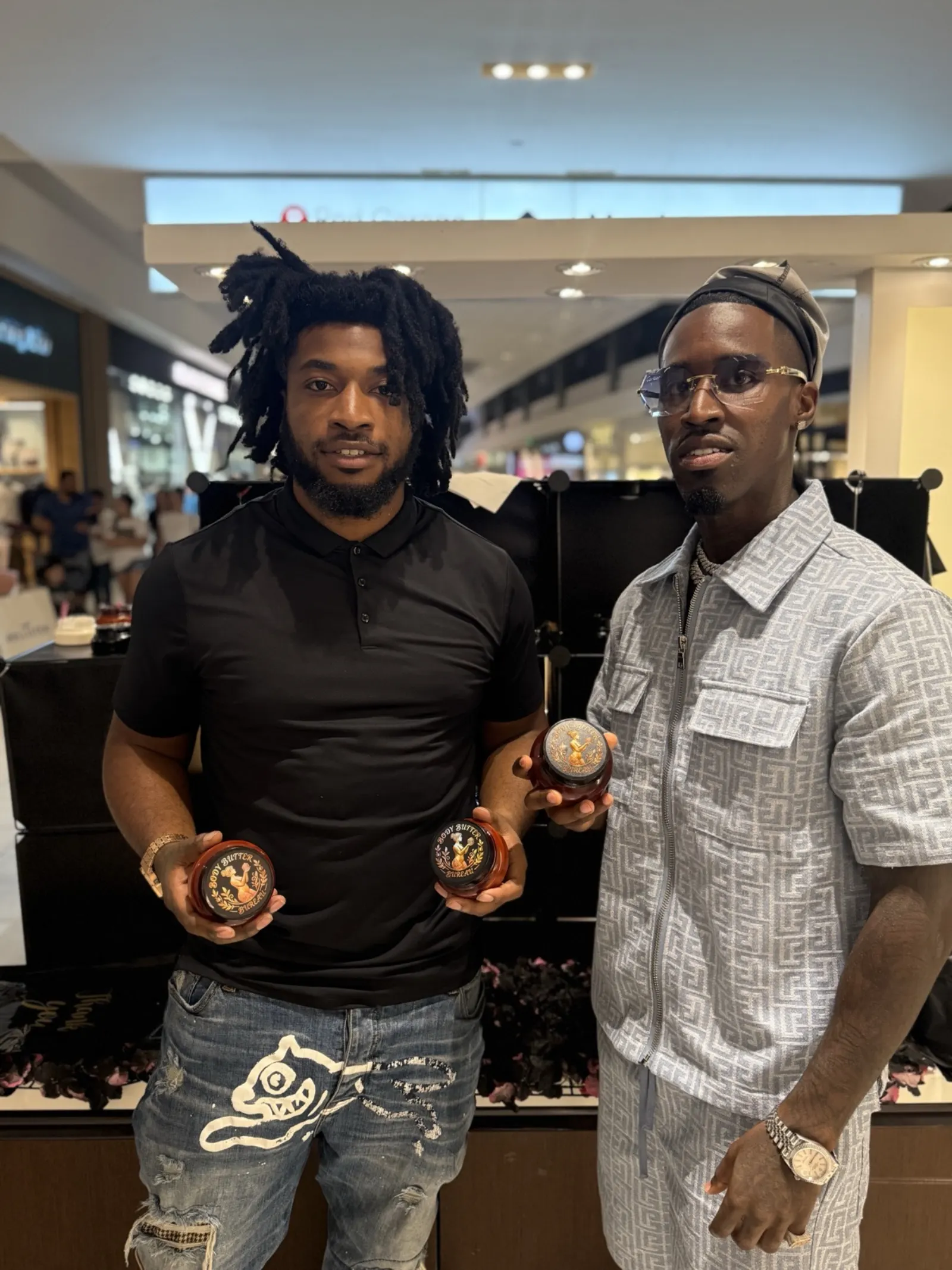 The two founders of Body Butter Bureau holding jars at their Galleria kiosk